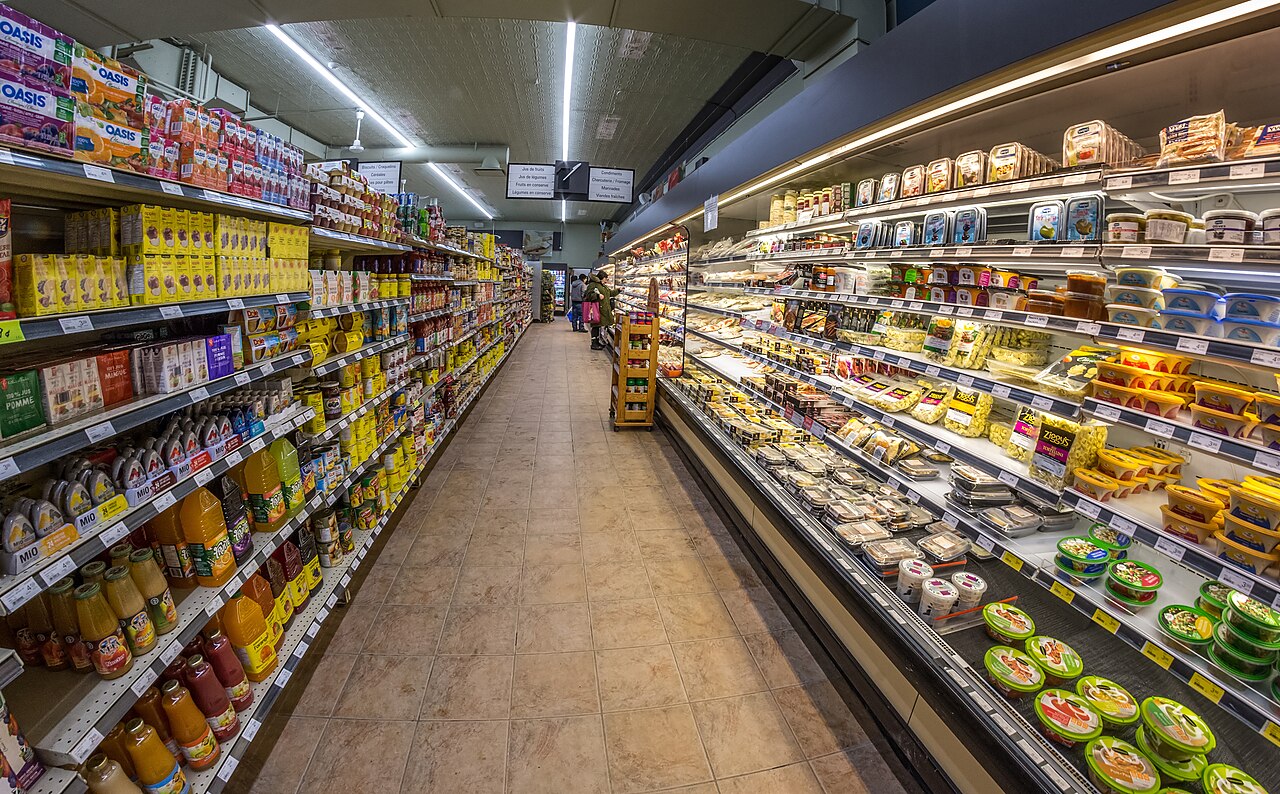 Corredor de supermercado com gôndolas e expositores abastecidos.